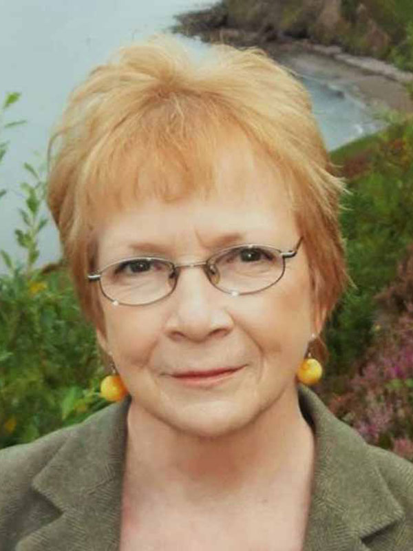 A headshot of Anya Peterson Royce, who wears a green blazer and round earrings.