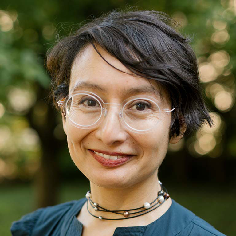 A headshot of Professor Sonia Velázquez, who poses outside and wears a teal shirt and a beaded necklace.