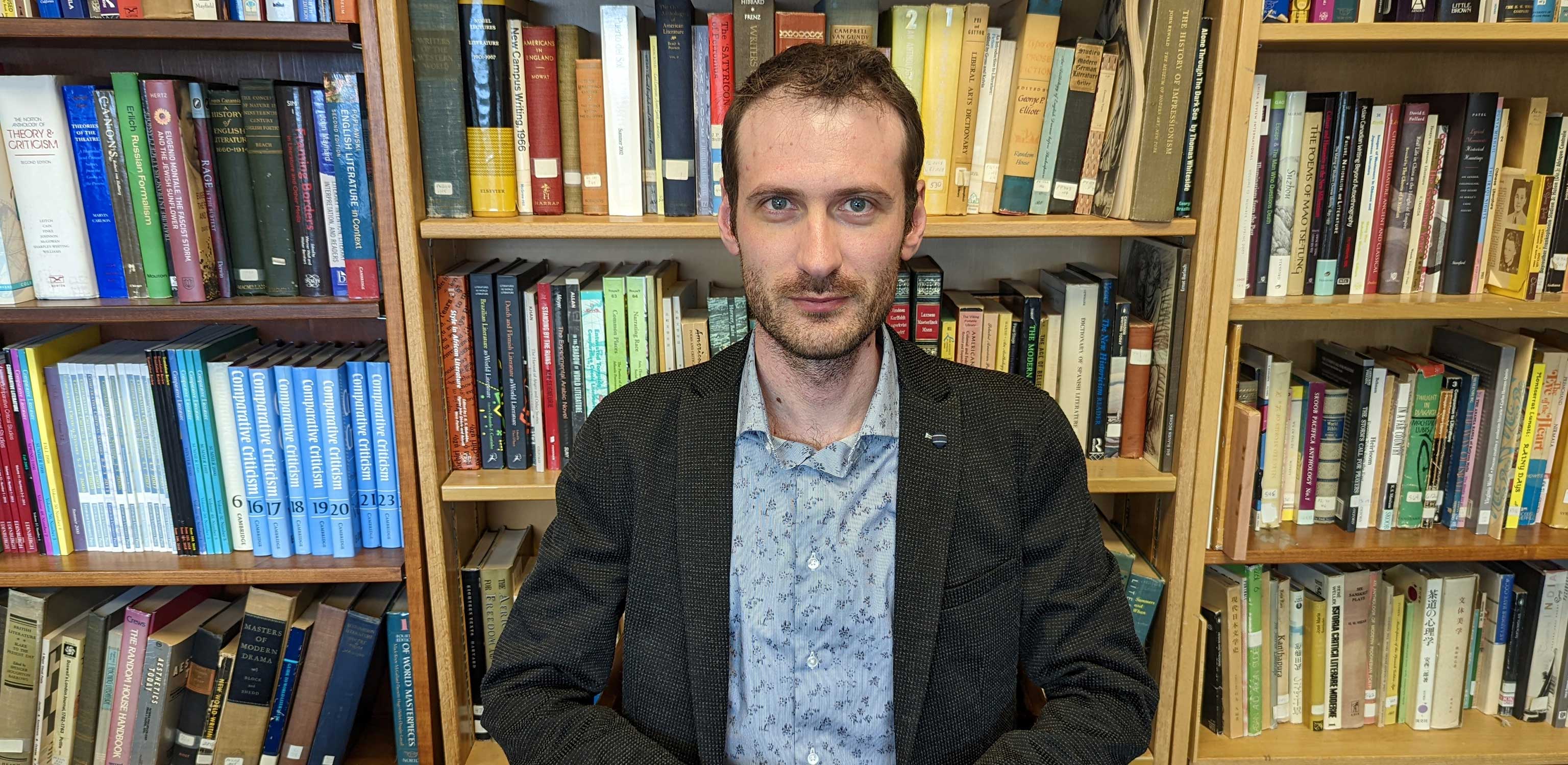 Alex Messejnikov poses in front of a bookshelf crowded with colorful books.