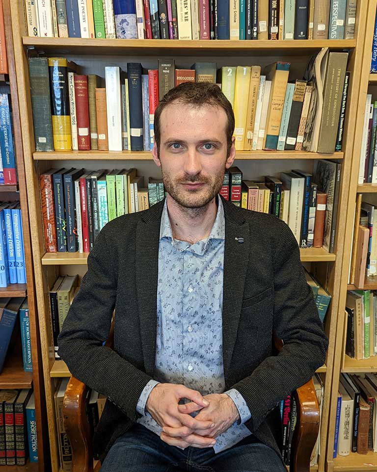 Alex Messejnikov poses in front of a large bookshelf crowded with colorful books.
